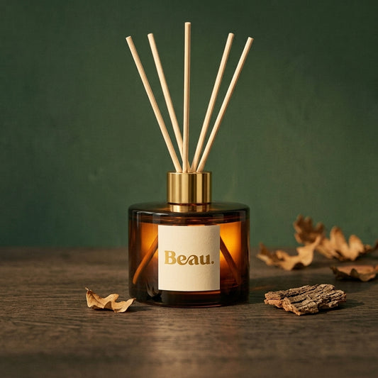 Cuban Tobacco & Oak reed diffuser in amber glass with a gold cap, on dark oak with dried oak leaves